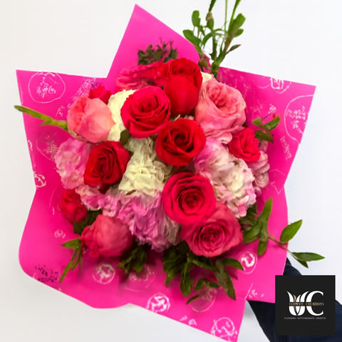 A bright bouquet of red, pink, and blush roses wrapped in vivid pink paper.