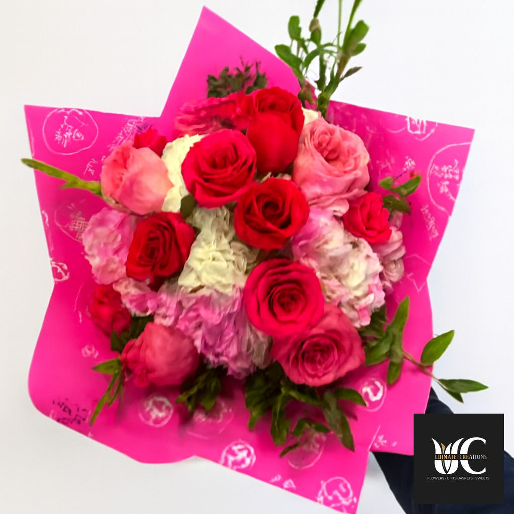 A bright bouquet of red, pink, and blush roses wrapped in vivid pink paper.