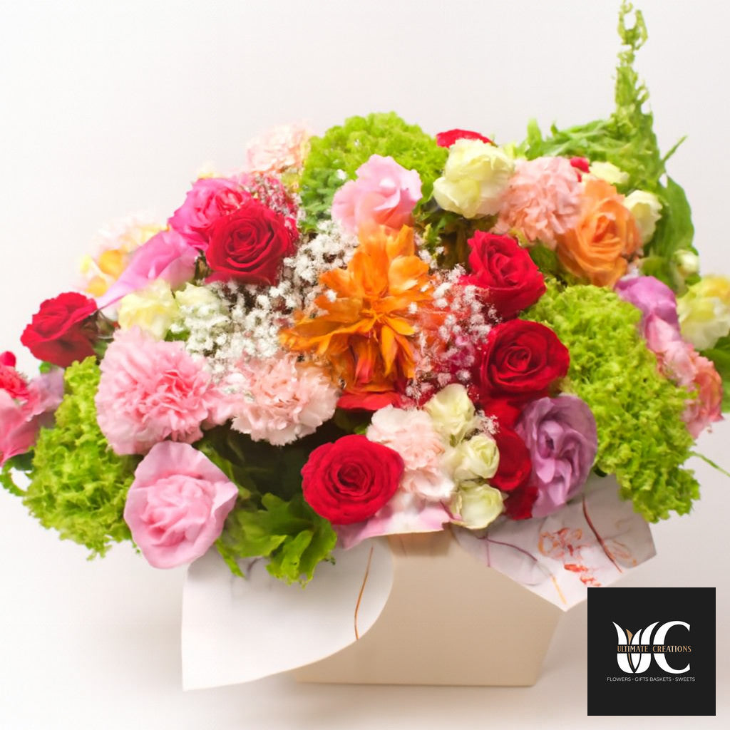 Colorful boxed floral arrangement with roses and mixed blooms in pink, red, orange, white, and green.