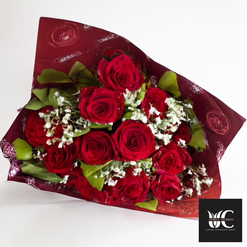Bouquet of red roses with green leaves and white filler wrapped in burgundy paper.