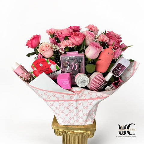 Pink rose bouquet wrapped in patterned paper and arranged with assorted beauty products in a floral gift display.