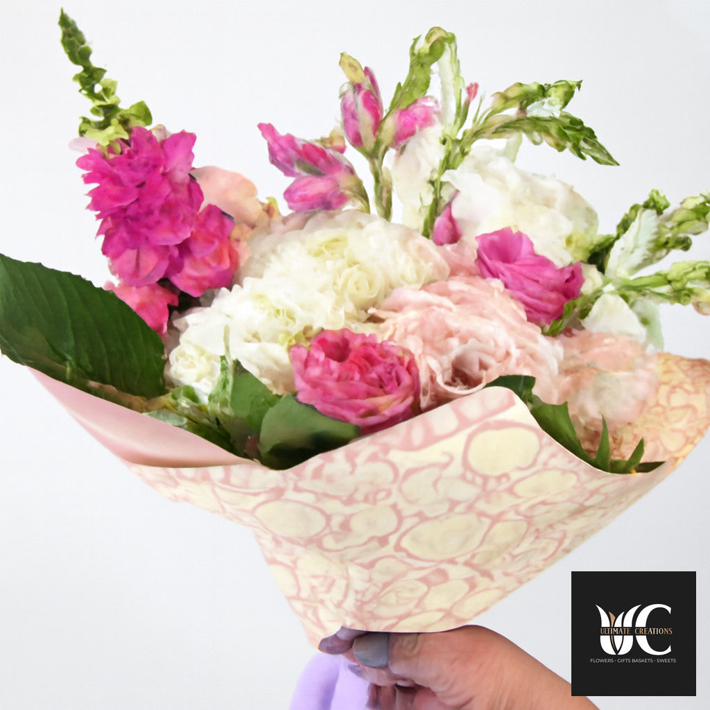 Hand-tied bouquet of pink and white flowers with greenery wrapped in patterned pink paper.