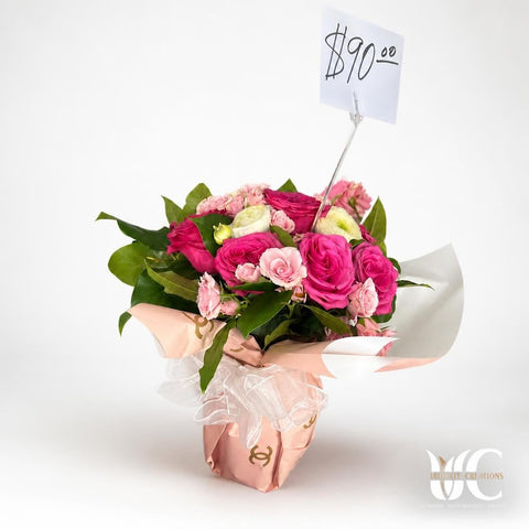 Lush bouquet of pink and blush flowers with pale green-white blooms and green foliage, wrapped in blush and white paper with a white bow.