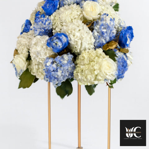 Blue and white floral centerpiece arranged on a tall gold stand.