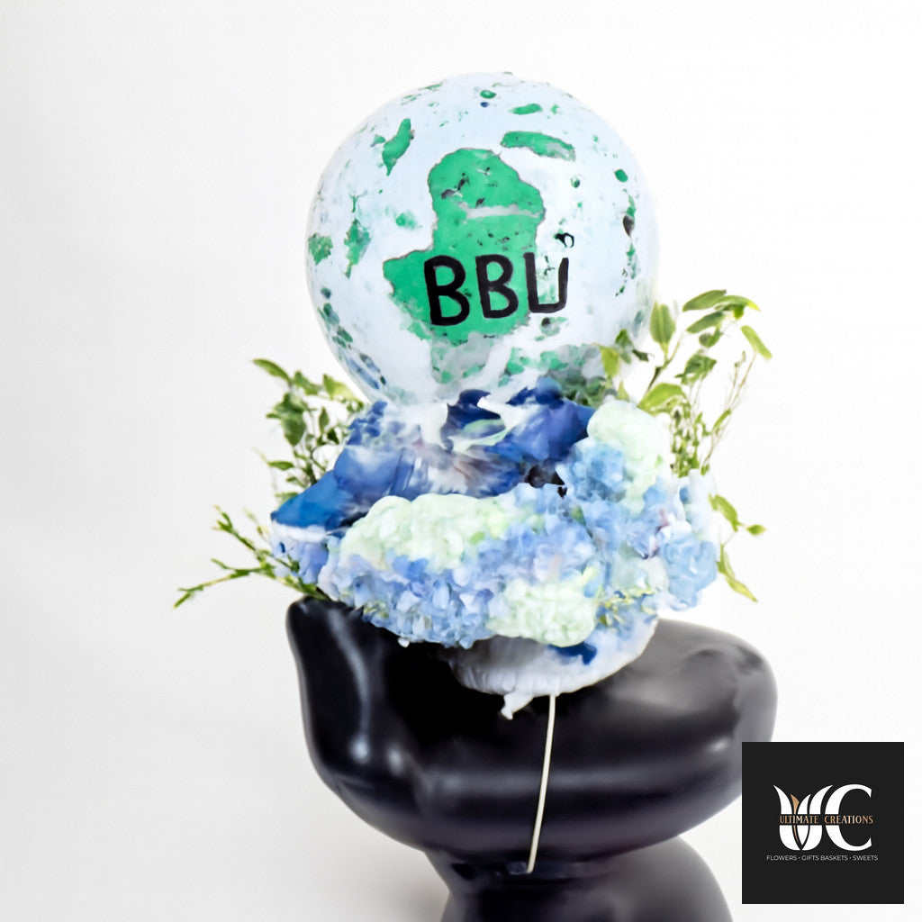 Balloon arrangement with a globe-style top balloon, blue and white flowers, greenery, and a black base.