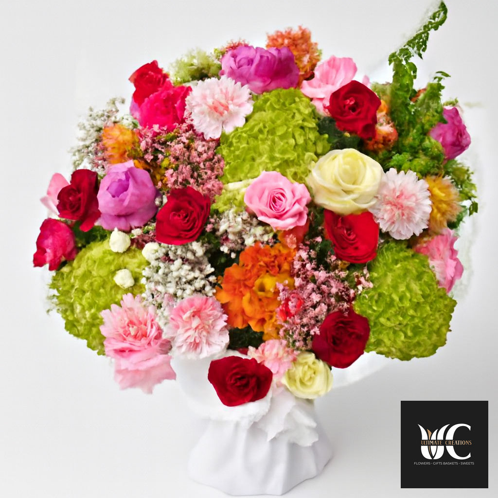 Colorful mixed flower arrangement in a white vase with roses, hydrangea, and filler flowers in pink, red, green, white, and orange.