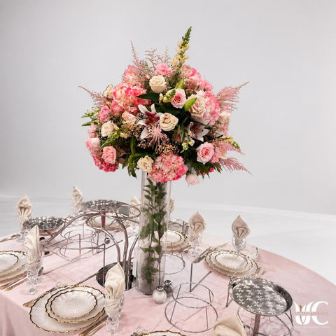 Tall blush and cream floral centerpiece in a clear glass vase on a formal pink table setting