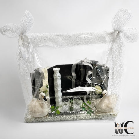 Enclosed white mesh gift arrangement with swan figures, glassware, greenery, and black-and-white decorative pieces