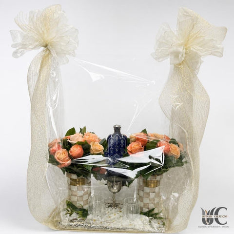 Two rose arrangements in a clear-wrapped gift display with large ivory bows and a decorative base.