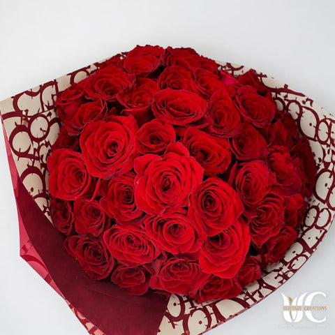 Dense bouquet of red roses wrapped in cream paper printed with burgundy lettering, viewed from above against a light surface.