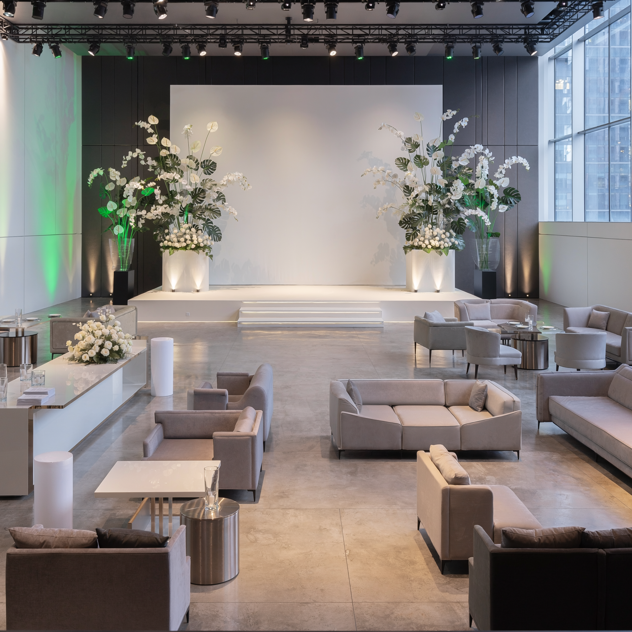 Modern corporate event stage with large floral installations, lounge furniture, uplighting and presentation backdrop