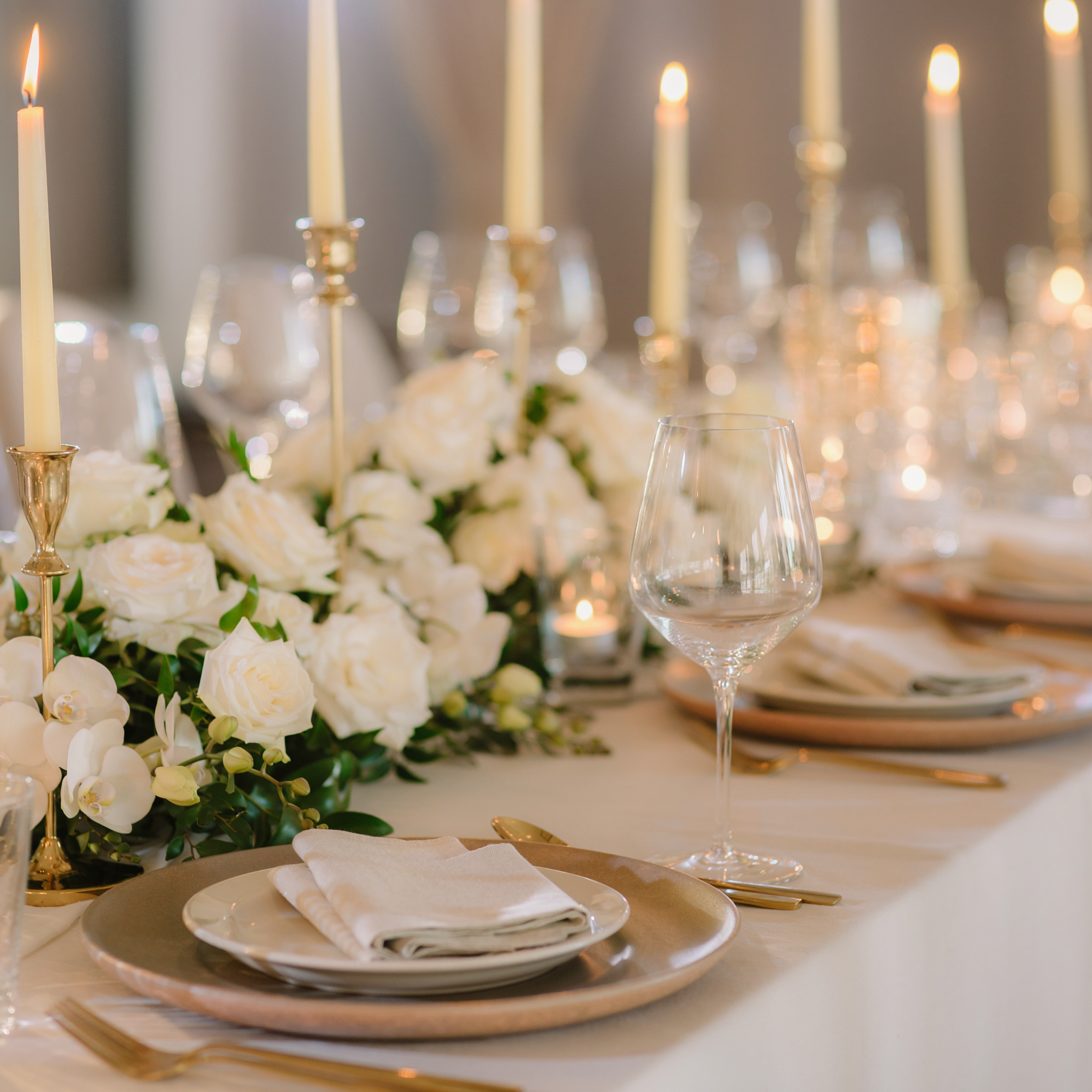 Elegant event tablescape with white floral centerpiece, candlelight, gold place settings and refined glassware